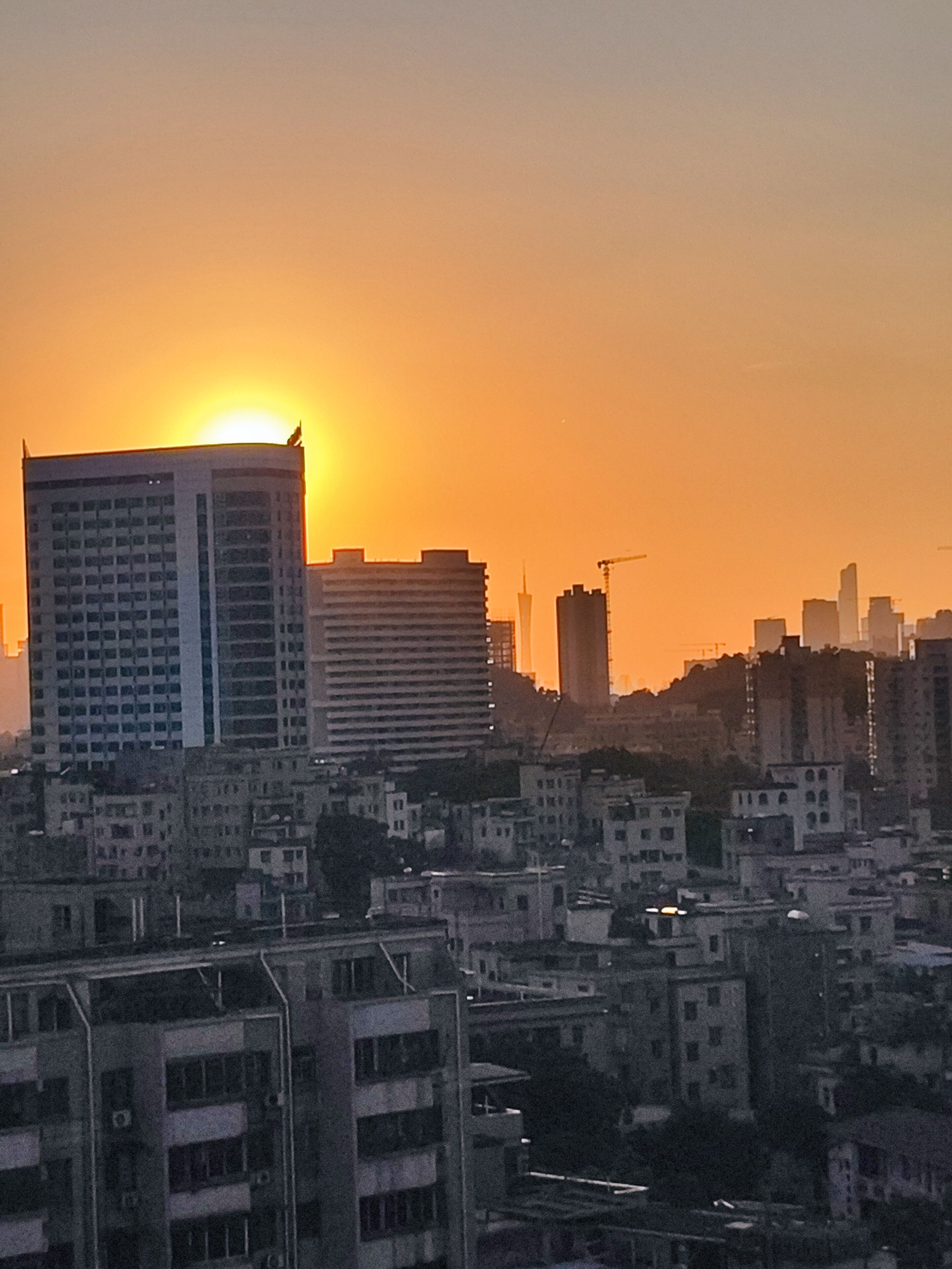 A cityscape at sunset with high-rise buildings and a construction crane.