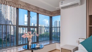 A hotel room with a large window, a small table with a vase, a bed, and a nightstand. - Guangzhou Hantao International Apartment (Guangzhou)