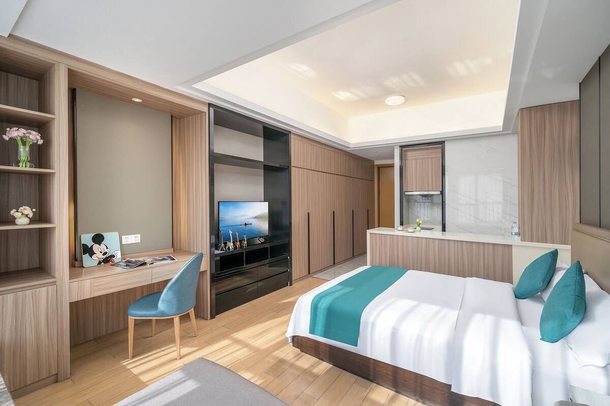 A modern hotel room with a desk, bed, TV, and built-in wardrobe.