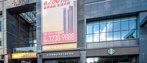 A modern building with a Starbucks Coffee shop, a large billboard advertising a property, and a sign indicating the direction to the mall.