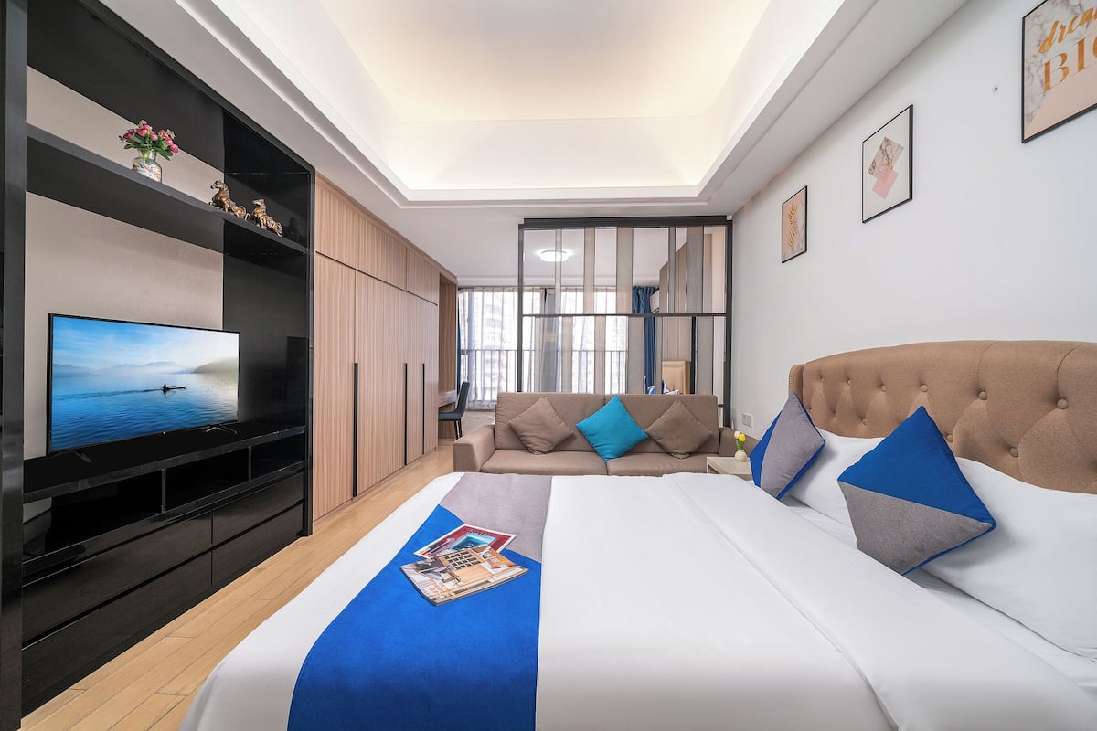 A modern hotel room with a large bed, a flat-screen TV, a sofa, and a minibar.