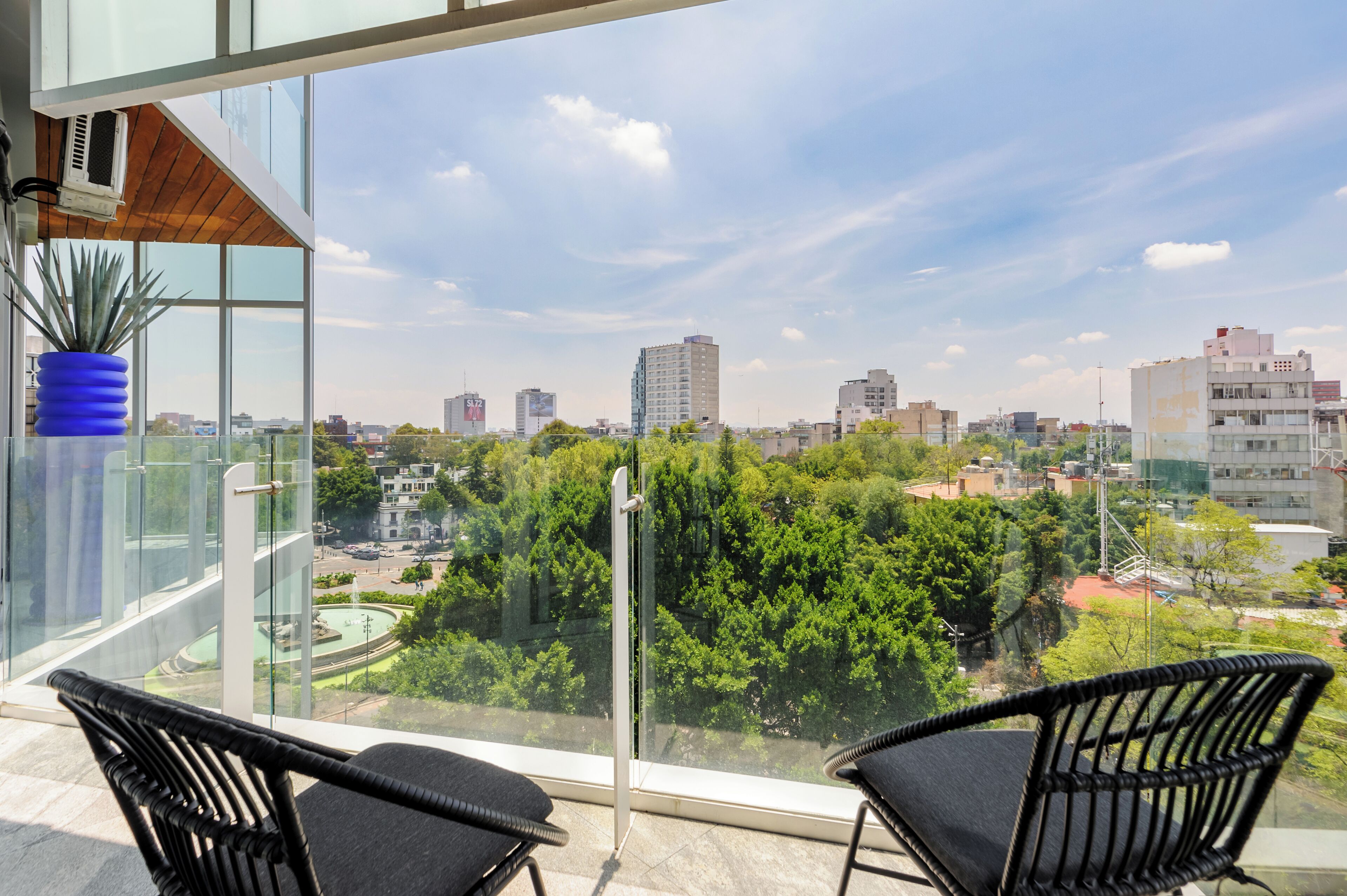 A balcony with two black wicker chairs, a blue vase, and a city view.