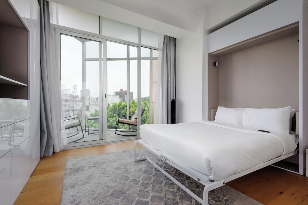 A modern bedroom with a bed, a view through a large window, and a balcony.