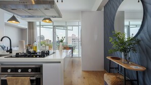 Eine moderne Küche mit einer zentralen Kochinsel, Edelstahlgeräten und Blick auf die Stadt durch große Fenster.