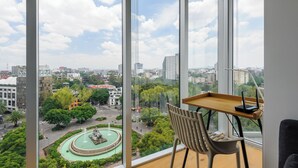 Ein modernes Zimmer mit großem Fenster und Blick auf eine Stadtlandschaft, eine Kreisverkehr und einen Brunnen.