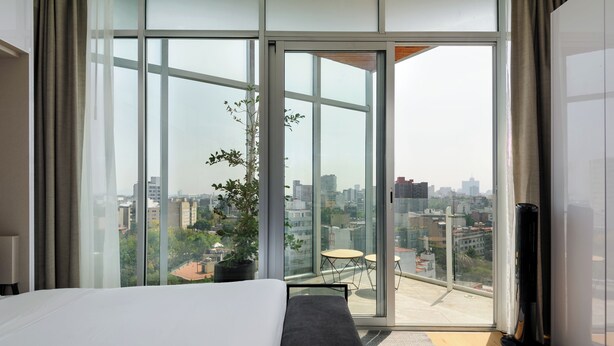 Ein modernes Hotelzimmer mit einer großen Schiebeglasdoor, die auf einen Balkon mit Blick auf die Stadt führt.