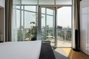 A modern hotel room with a large sliding glass door leading to a balcony with a city view. - Icon Cibeles by Wynwood House (Mexico City)
