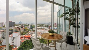 Ein Balkon mit Holztisch und -stühlen, einem Blumentopf und Blick auf die Stadt.