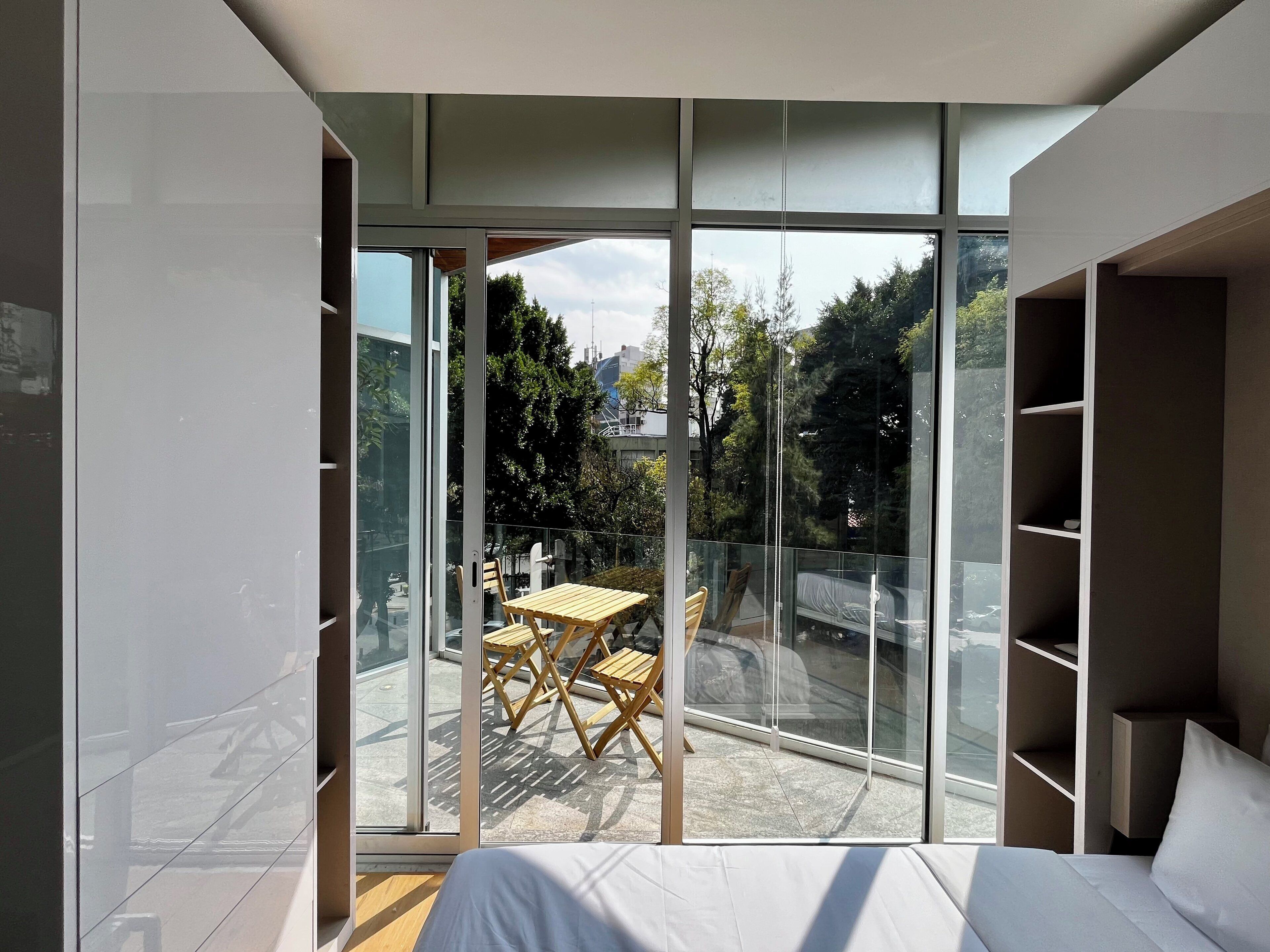 Una camera da letto moderna con ampie vetrate, un tavolo e sedie in legno all'esterno e scaffalature a muro.
