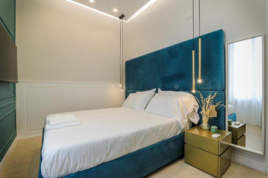 A modern bedroom with a large bed, a nightstand, a mirror, and a vase with dried plants.
