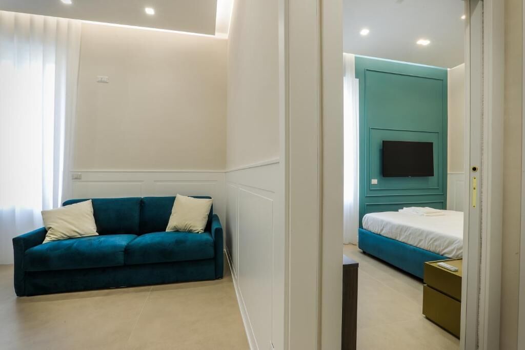 Una camera da letto moderna con un divano color acquamarina, un letto con testiera coordinata nello stesso colore e una TV a schermo piatto montata a parete.