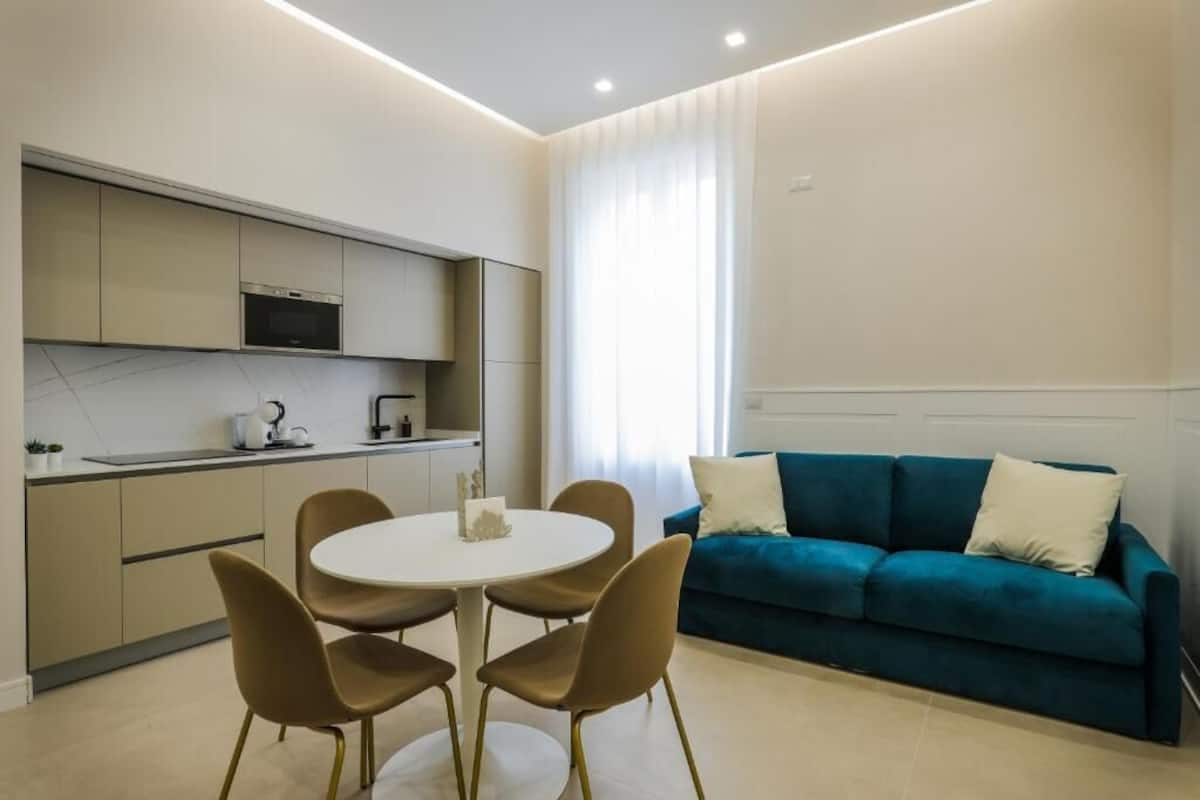 A modern kitchen with a dining area, a teal sofa, and a small table with chairs.