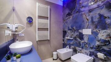 A modern bathroom with a large white sink, a bidet, and a toilet. There are small potted plants on the counter.