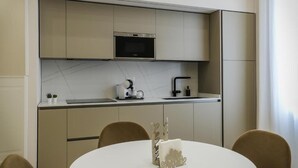 A modern kitchen with a microwave, coffee maker, and sink. There is a dining table with chairs and a decorative item on it. - Conte Relais Suite (Naples)