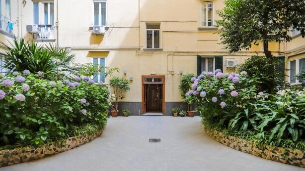 A courtyard with a central entrance, surrounded by potted plants and flowers. - Conte Relais Suite (Naples)