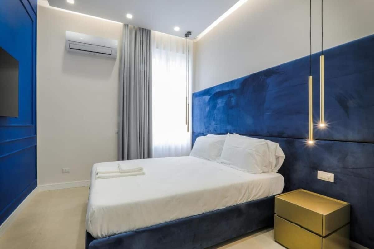 A modern bedroom with a large bed, a nightstand, and a wall-mounted air conditioner.