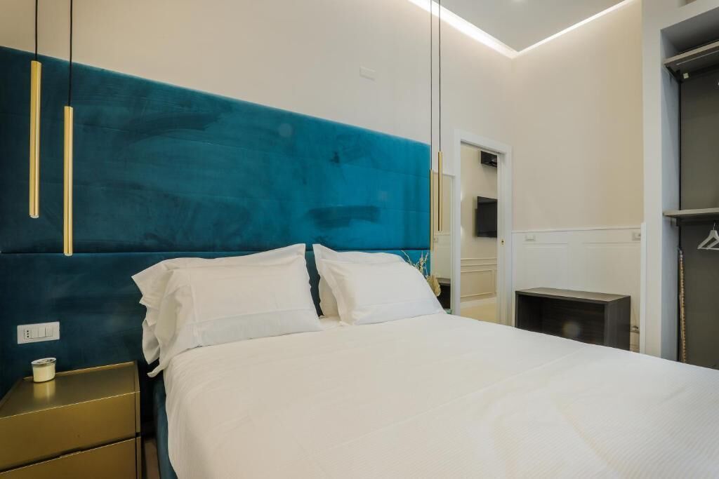 A modern hotel room with a large bed, a bedside table, a wardrobe, and a mirror.