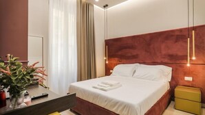 A modern hotel room with a large bed, a bedside table, a nightstand, and a desk with a chair. - Conte Relais Suite (Naples)