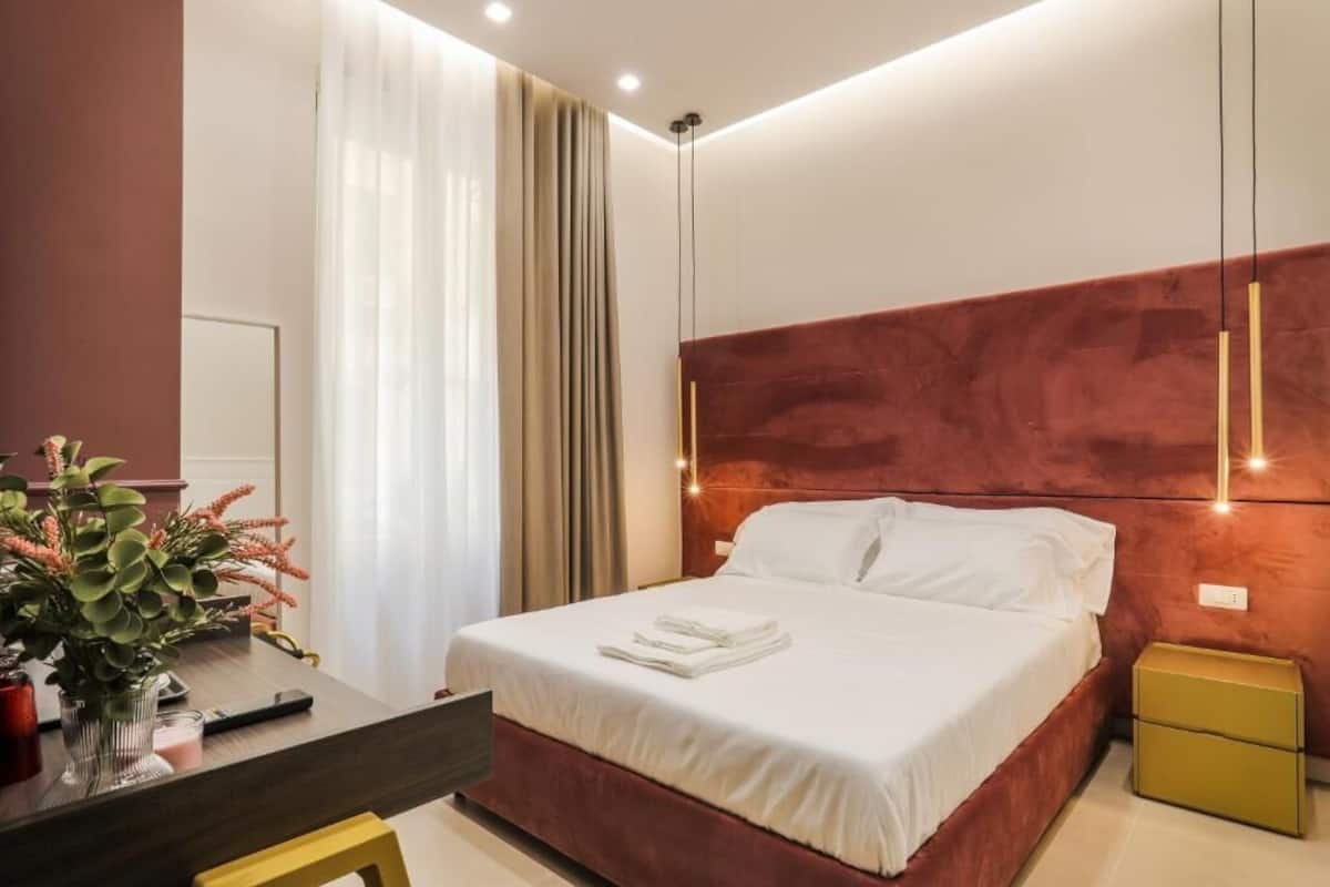 A modern hotel room with a large bed, a bedside table, a nightstand, and a desk with a chair.