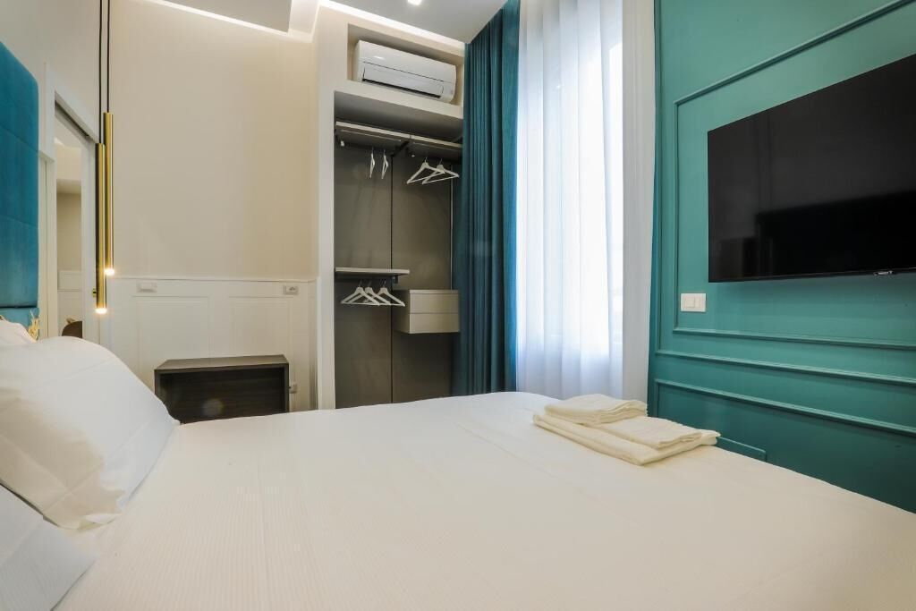 A hotel room with a bed, a wardrobe, a TV, and an air conditioning unit.