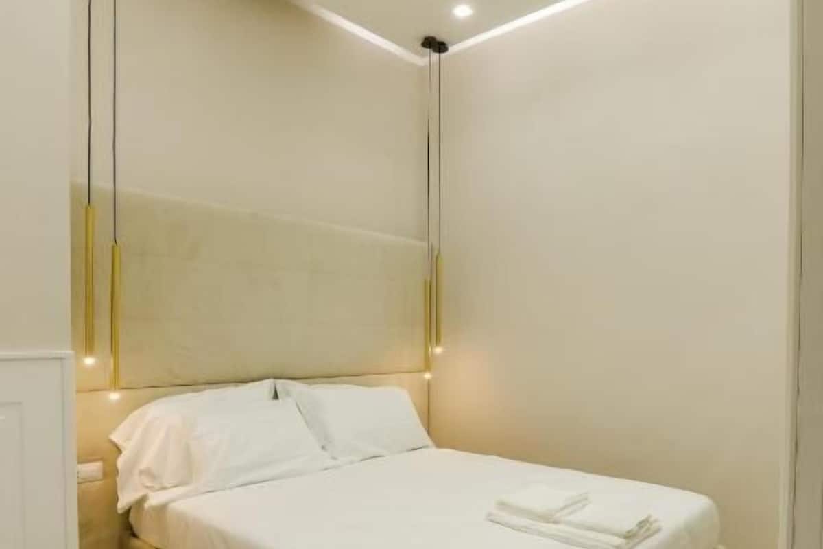 A modern bedroom with a bed, bedside tables, and recessed ceiling lighting.