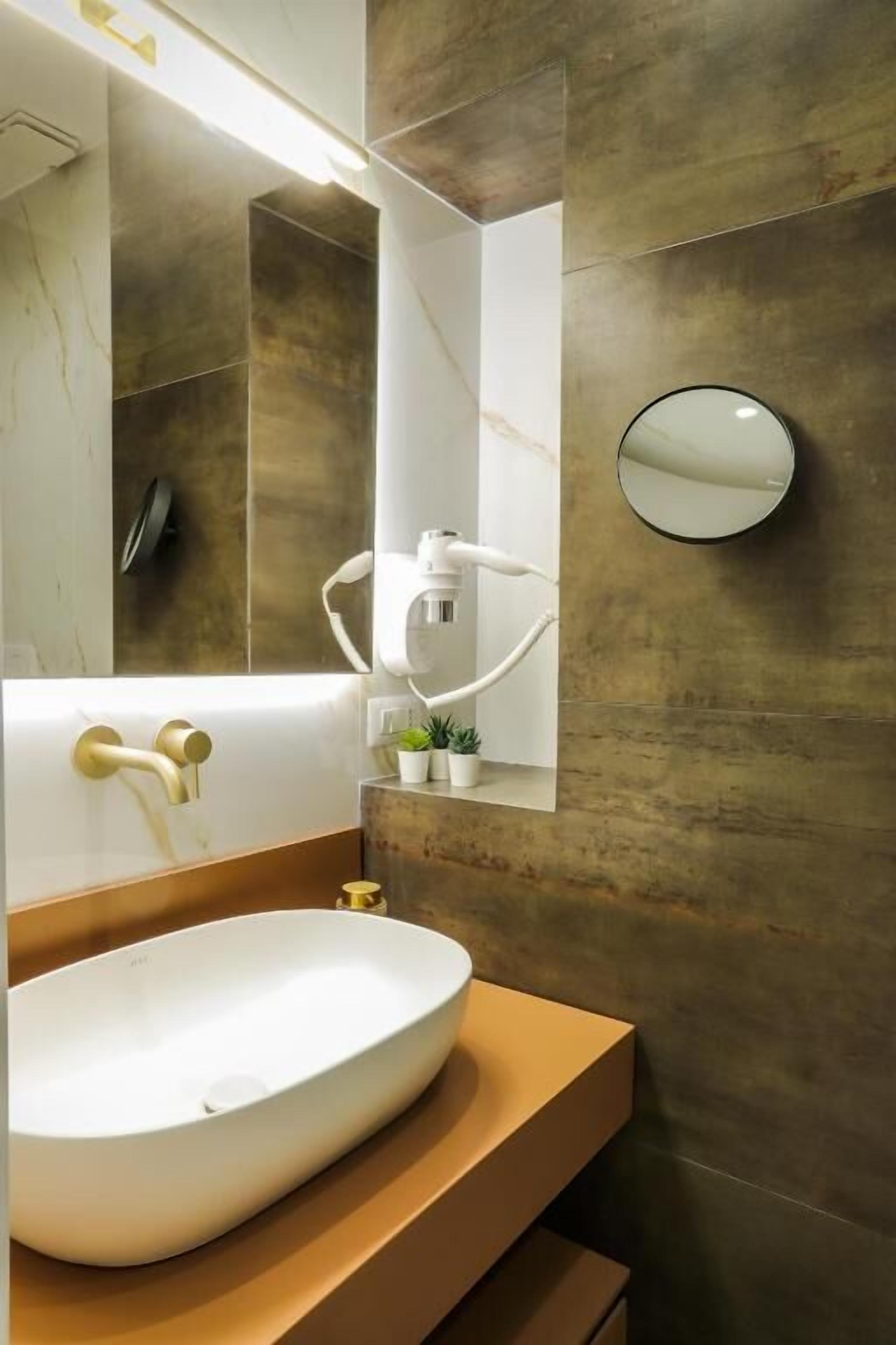 A modern bathroom with a large oval sink, a wall-mounted mirror, and a small potted plant.