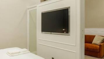 Una camera da letto moderna con un letto, una TV fissata a parete e una porta scorrevole che dà su un'altra stanza.