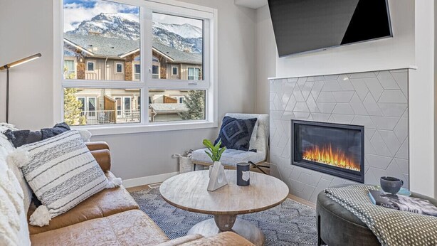 Ein modernes Wohnzimmer mit Kamin, einem großen Fenster mit Blick auf die Berge und einer gemütlichen Sitzecke.