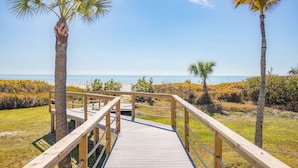 A wooden boardwalk leading to a beach with palm trees and a clear blue sky.
