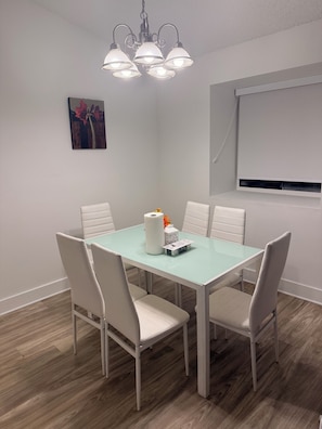 Een eetgedeelte met een tafel, stoelen, een kroonluchter, een schilderij en een raam.