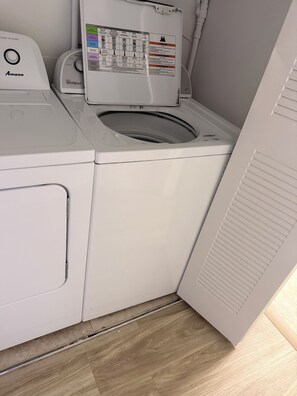 Un appareil combiné lave-linge et sèche-linge à chargement frontal, doté d’un panneau de commande, du logo Whirlpool et d’une étiquette indiquant les consignes de sécurité.
