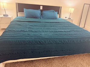 A bed with a teal bedspread, two pillows, a nightstand with a lamp, and a wall-mounted clock. - Stay close to shopping paradise! Apartment near Sawgrass and Hardrock stadium (Plantation)