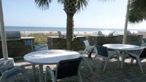 Een buitenzitgedeelte met tafels en stoelen, met uitzicht op een strand.