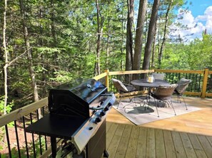 Una terraza al aire libre con una parrilla, una mesa redonda y sillas.