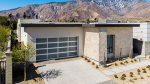 A modern building with a garage, surrounded by a landscaped garden and a mountain backdrop. - Posh Private Panoramic View Compound w/Pool & Spa (Palm Springs)