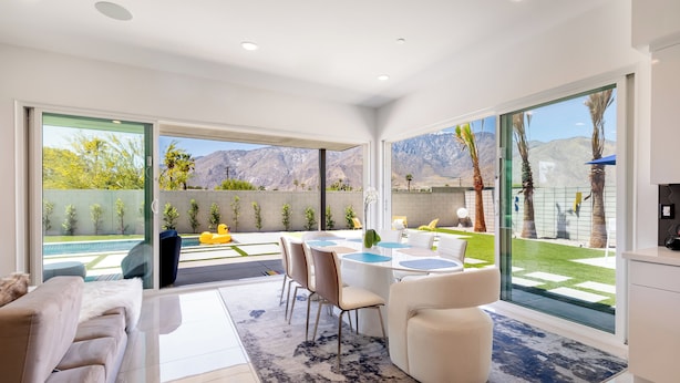 A modern living room with a large window, a dining area with a table and chairs, and a sofa. - Posh Private Panoramic View Compound w/Pool & Spa (Palm Springs)