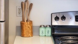 Een keuken met een fornuis, houten keukengerei in een pot en twee potten met initialen.