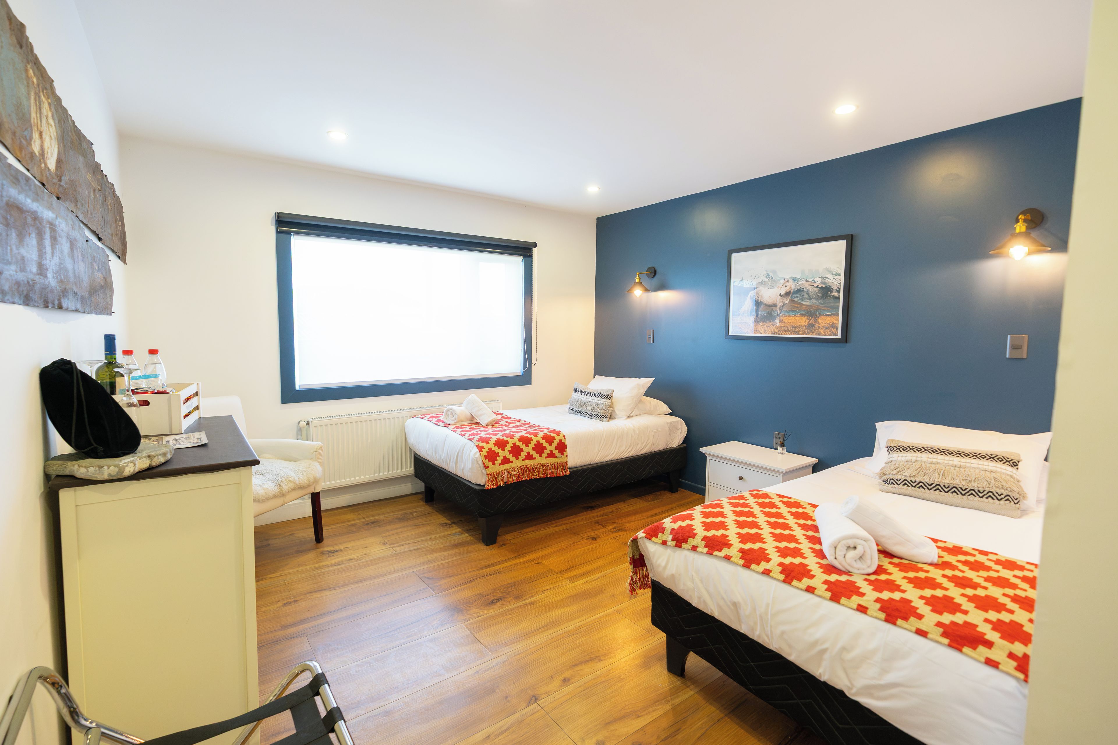 Una habitación de hotel con dos camas, un escritorio, una silla, una ventana y un cuadro en la pared.