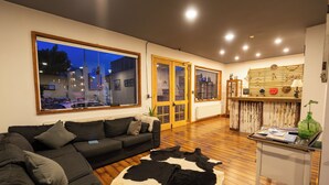 Ein Wohnzimmer mit großem Fenster, einer Couch, einem Kuhfellteppich und einem kleinen Tisch mit Lampe.