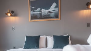 Ein Hotelzimmer mit einem Bett, Kissen, einer Decke, einem gerahmten Bild an der Wand und zwei Wandlampen.