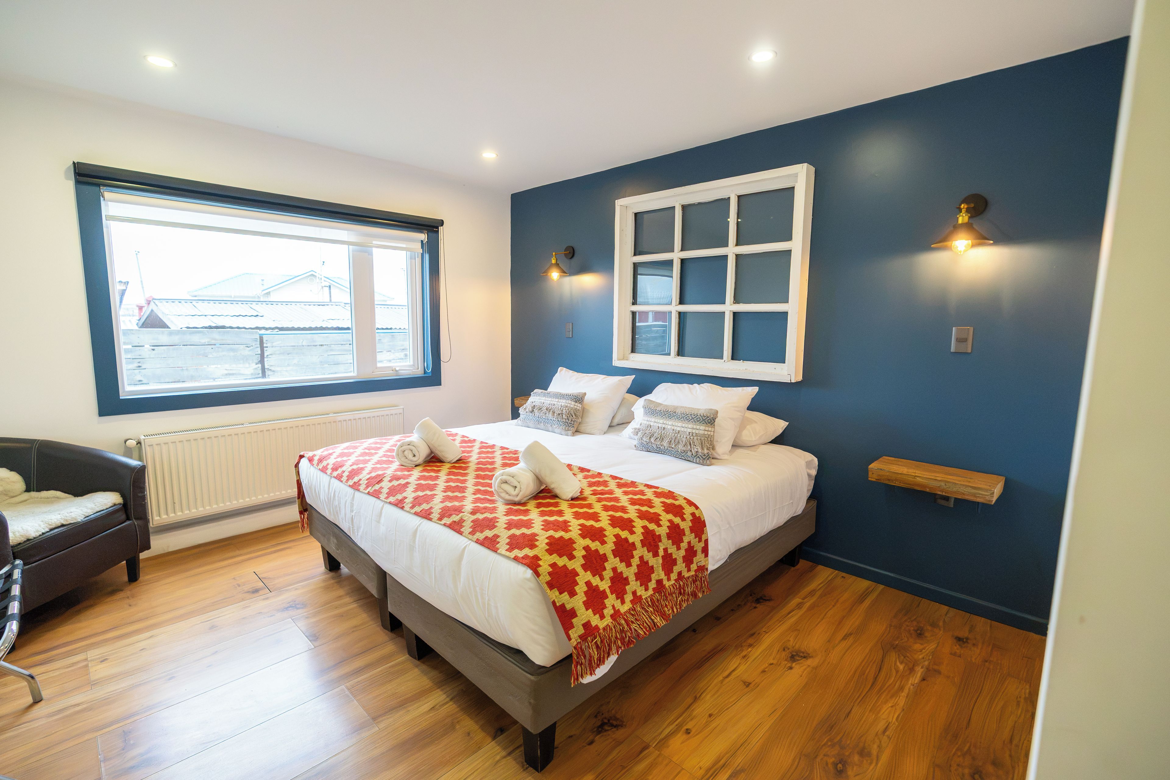 A bedroom with a large bed, a window, a radiator, and a chair.