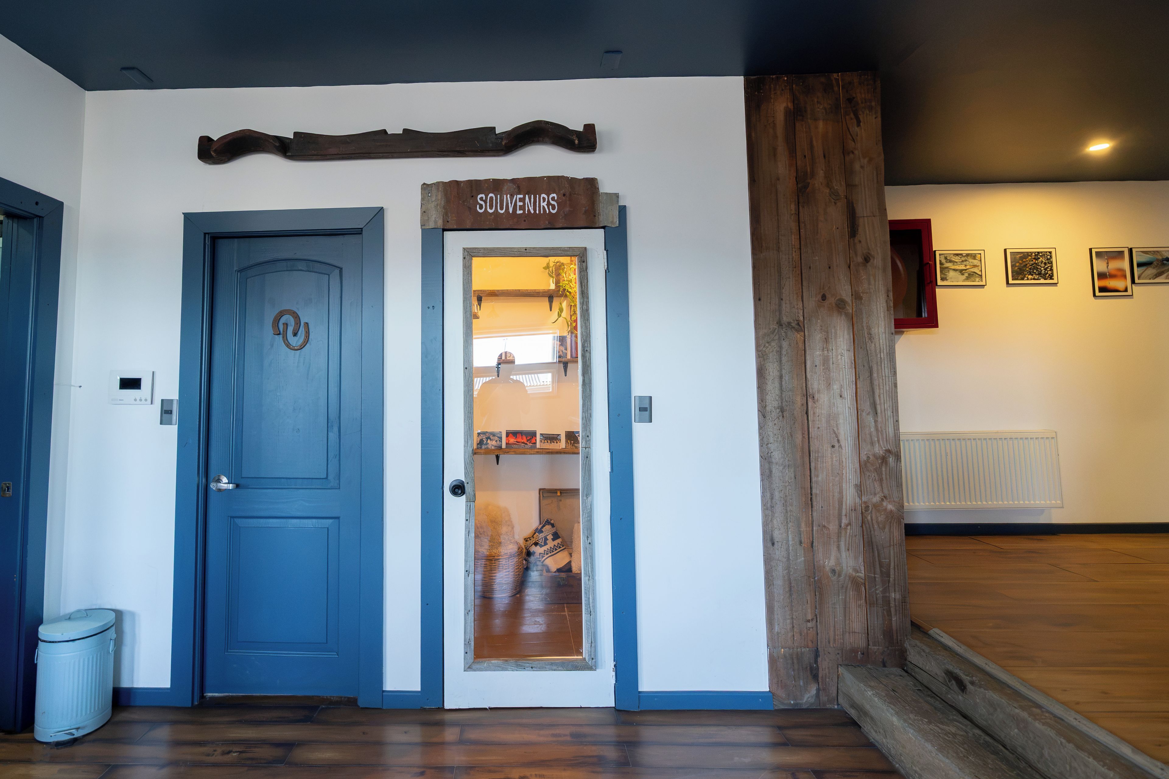 Una habitación con una puerta azul, un letrero de madera encima y una pared con cuadros enmarcados.