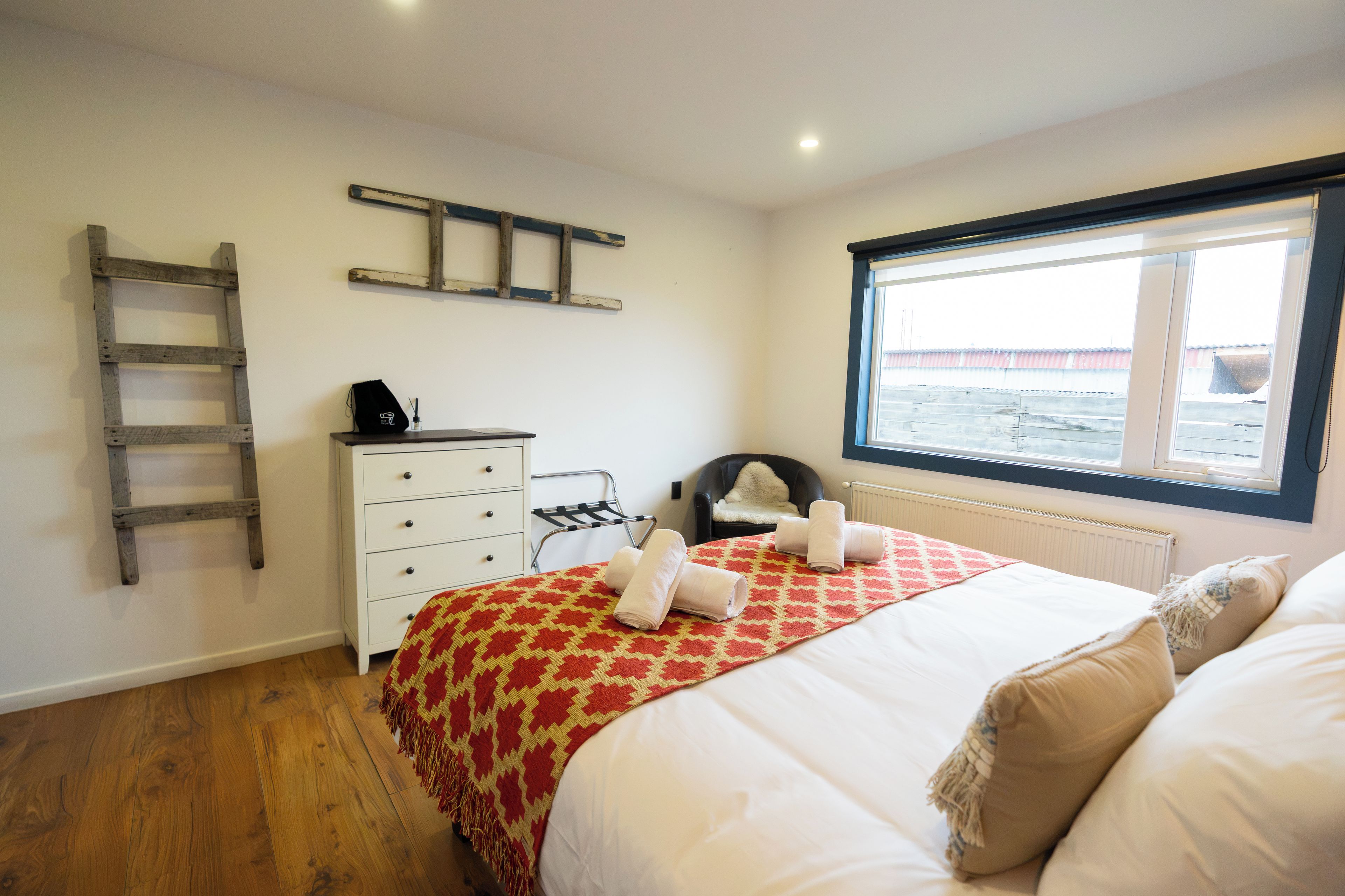 A bedroom with a bed, a dresser, a chair, a window, and a ladder.