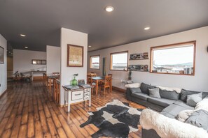 A spacious living area with a wooden floor, a gray sofa, a cowhide rug, and a dining area with wooden furniture. - Pristine Patagonia Hotel (Natales)