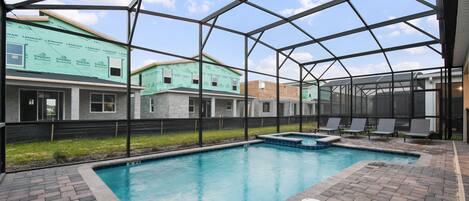 Una piscina con borde de ladrillo, rodeada por una valla metálica, con vista a edificios en construcción.