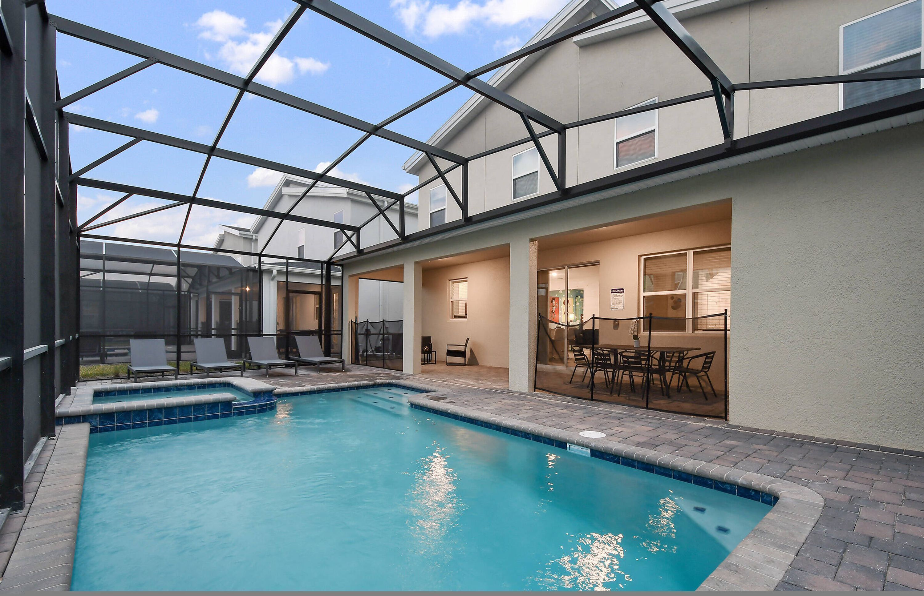 A swimming pool with a glass enclosure, lounge chairs, and a patio area with outdoor furniture.