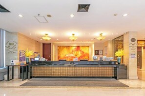 A hotel reception area with a reception desk, a large wall-mounted screen, and a modern ceiling design.