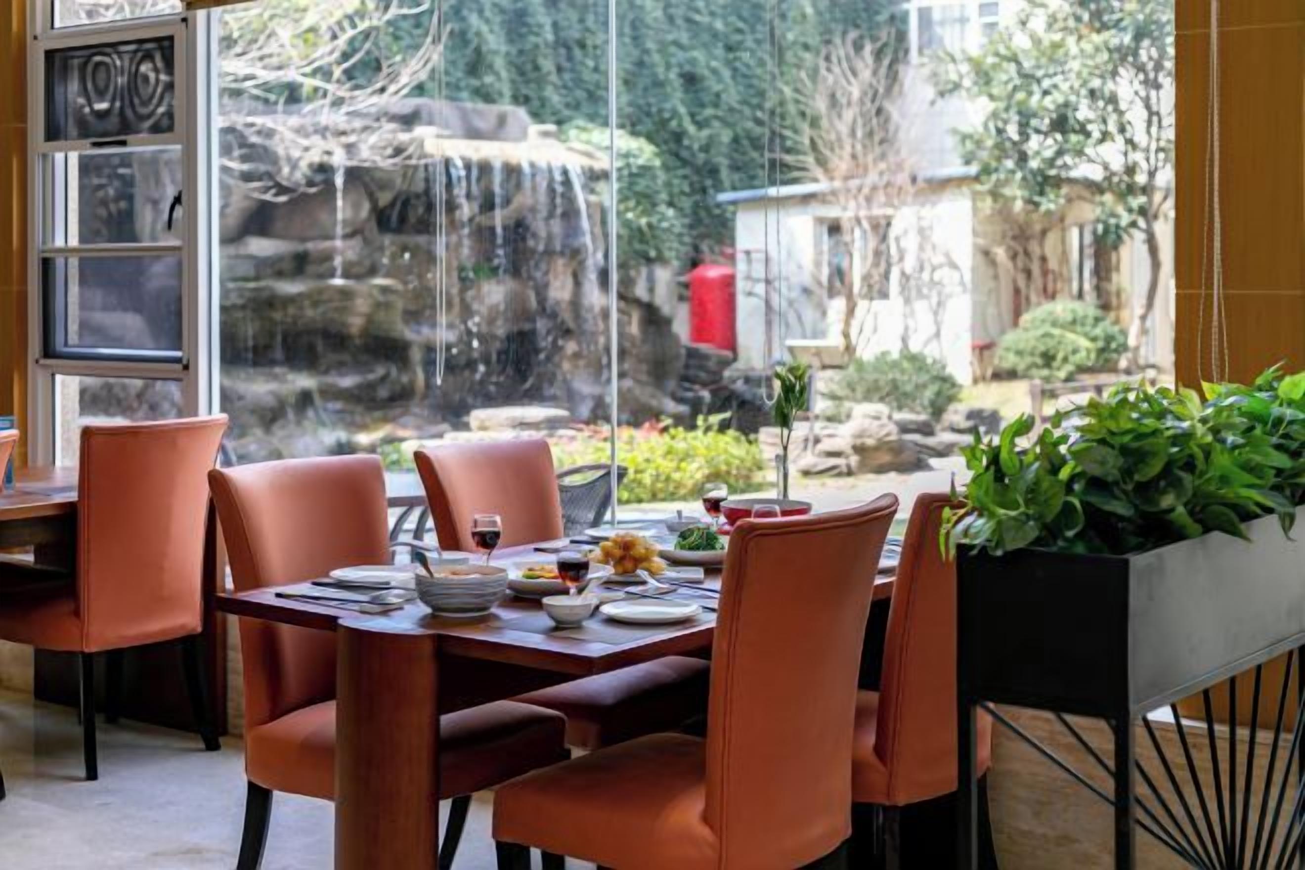 An indoor dining area with a table set for four, chairs, and a view of a waterfall outside.