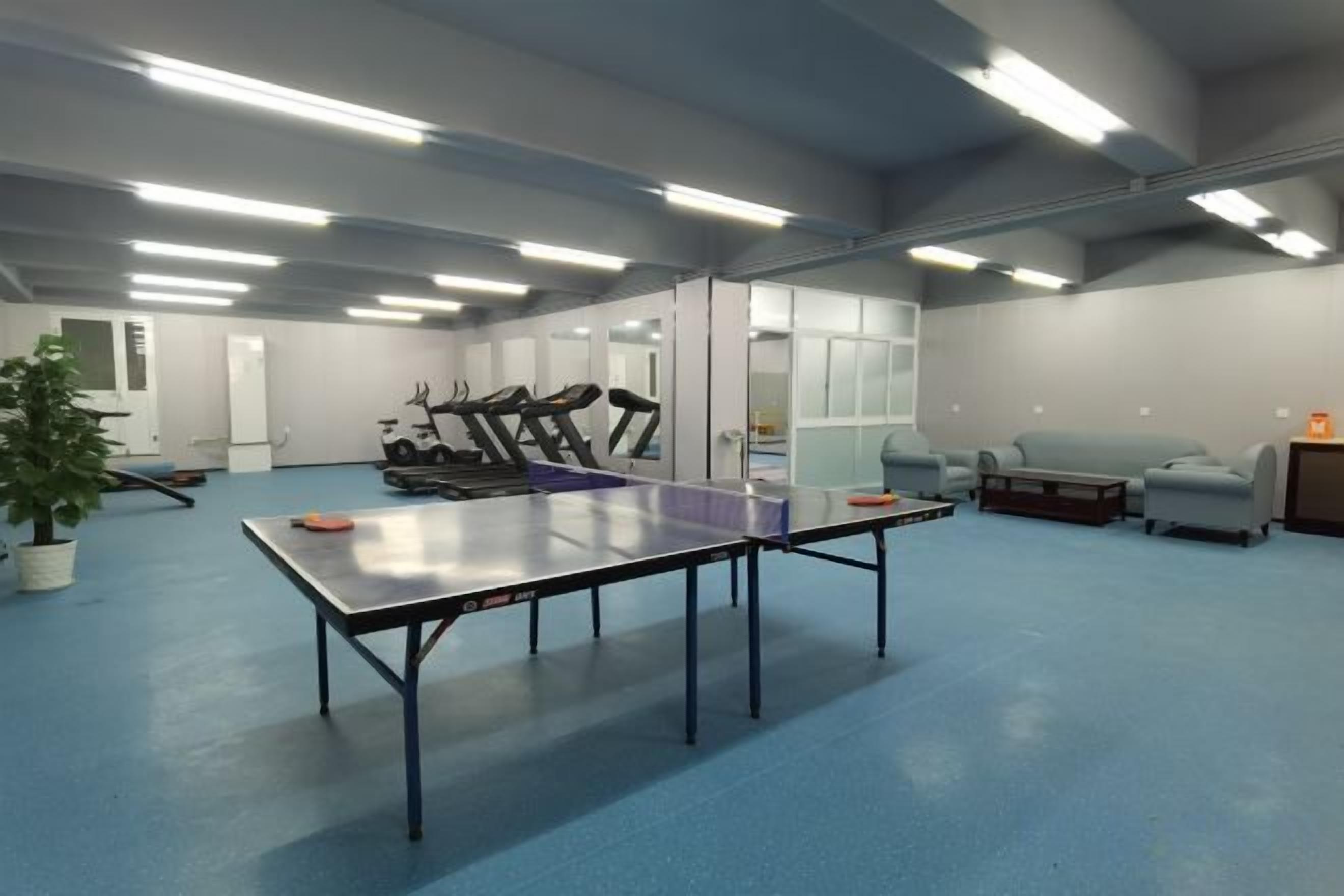 A spacious room with a ping pong table, exercise equipment, and seating areas.
