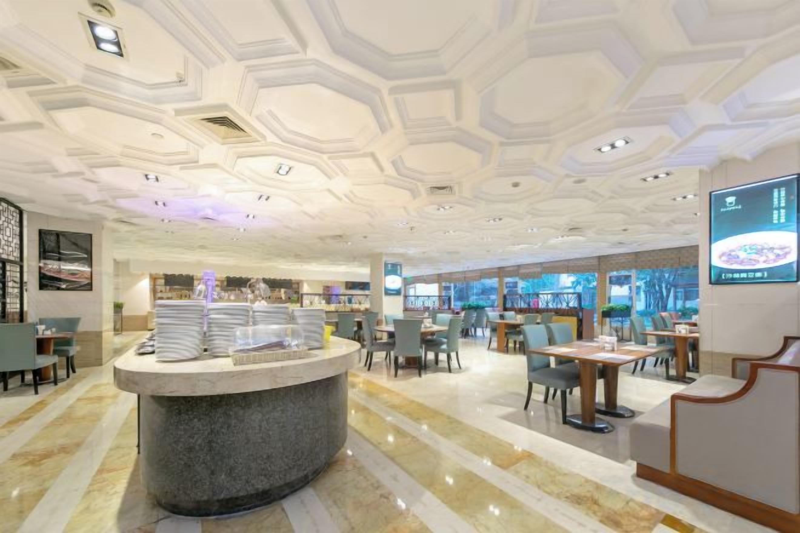Un hall d’hôtel comprenant un comptoir d’accueil central, un espace salon et un grand écran affichant des informations.